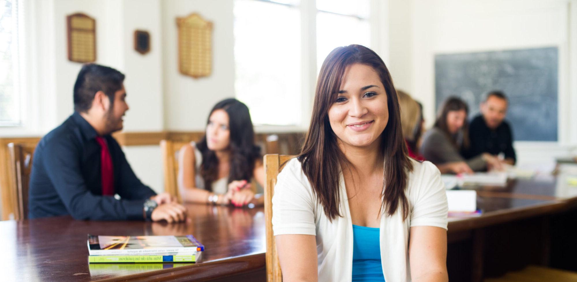 Female student smiling with college classmates at table behind her.