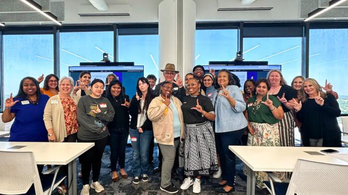 Attendees at the Culturally Relevant Literacy Seminar pose for a group photo while holding up the Lucky Lion hand gesture involving the right-hand thumb and first two fingers.